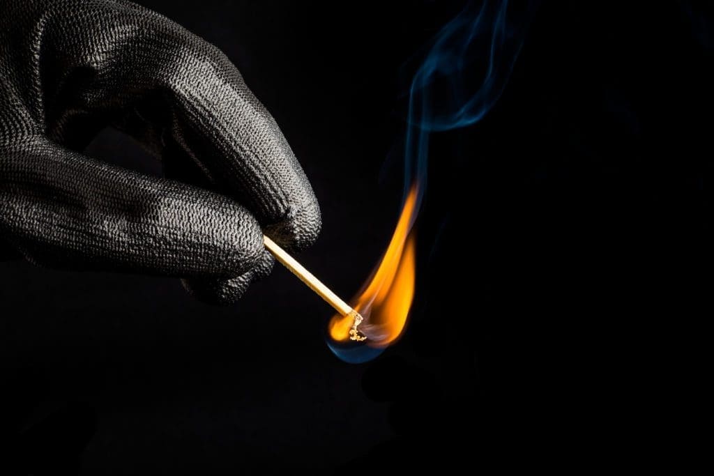 A gloved hand starts a match. Arson.